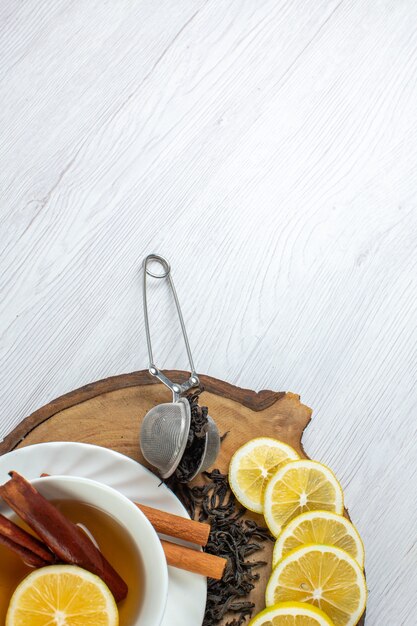 Vertical view of black tea in a white cup and lemon on a wooden tray on white background