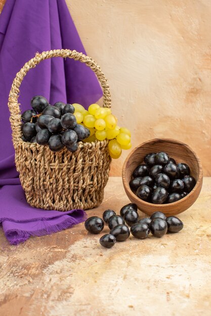 Vertical view of black and yellow fresh grapes fallen from small pot and in a wooden basket behind the purple towel