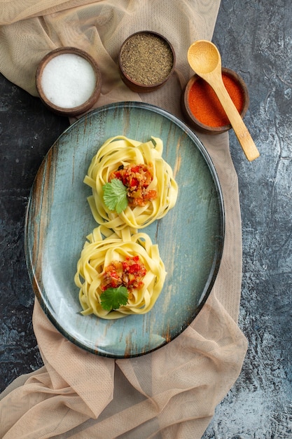 Вертикальный вид синей тарелки с вкусной пастой, подаваемой с помидорами и мясом на полотенце коричневого цвета на ужин с разными специями