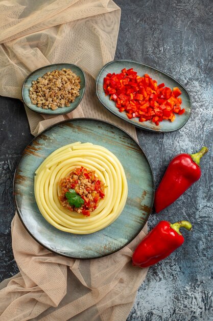 Vertical view of a blue plate with tasty pasta meal served with tomato and meat on tan color towel chopped and whole peppers