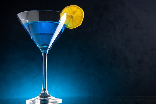 Vertical view of blue water in a glass goblet served with lemon slice on dark background