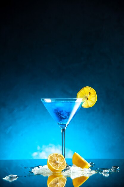 Vertical view of blue water in a glass goblet served with lemon slice and ice on dark background