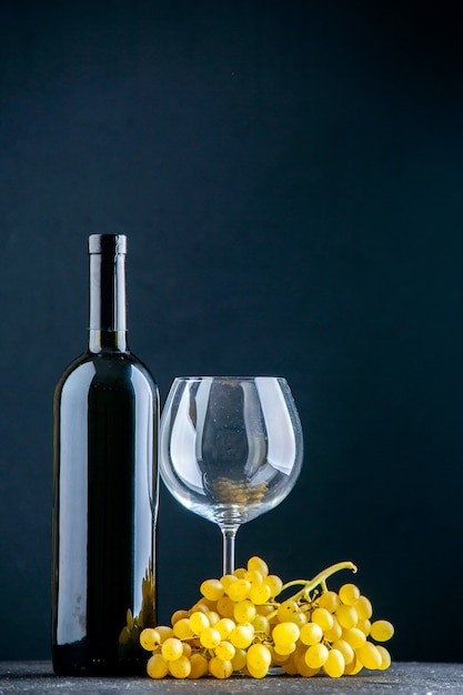 Vertical view of a bundle of yellow grape and bottle glass goblet on dark background