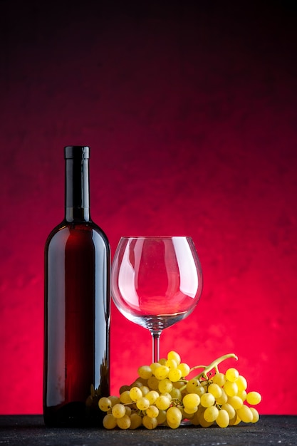 Vertical view of a bundle of yellow grape and bottle glass goblet on red background