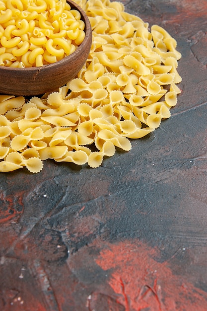 Free photo vertical view of butterfly uncooked pastas in a brown bowl on the right side of mixed color background