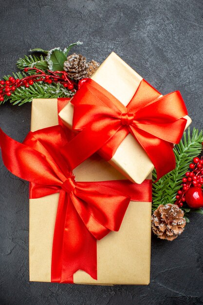 Foto gratuita vista verticale dell'atmosfera natalizia con bellissimi doni con nastro a forma di fiocco e accessori per la decorazione di rami di abete su uno sfondo scuro