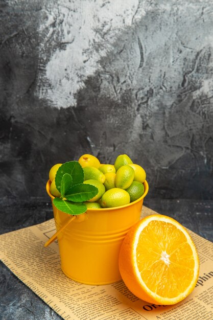 Vertical view of citrus fruits in a basket on newspaper on gray background