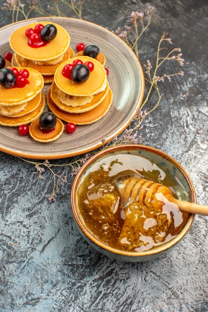 Free photo vertical view of classic fruit pancakes and honey in a bowl