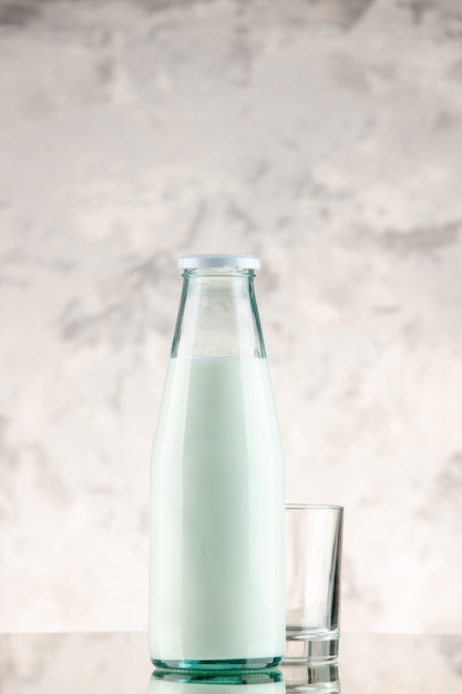 Vertical view of closed and filled with milk glass bottle and cup on white smoke wall with free space