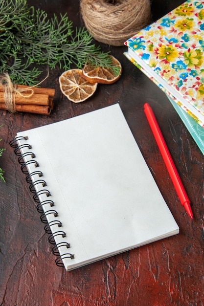 Vertical view of closed notebook with pen cinnamon limes a ball of rope and books on dark background