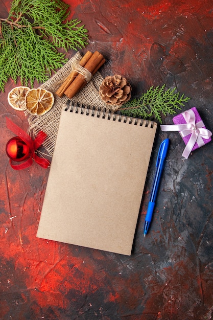 Vertical view of closed notebook with pen cinnamon limes gift conifer cone decoration accessory fir branche on dark background