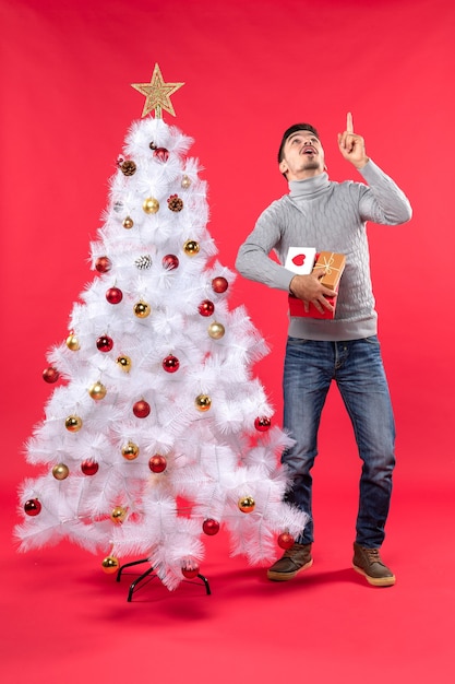 飾られた白いクリスマスツリーの近くに立っている混乱したハンサムな男の垂直方向のビュー