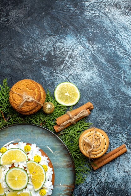 Vertical view of creamy delicious cake and fir branches lemon cinnamon limes on dark background