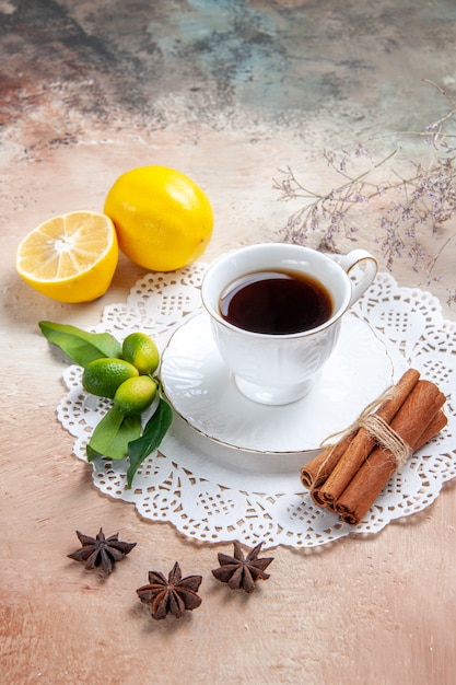 Vista verticale di una tazza di tè nero sul tovagliolo decorato con frutta cannella sul tavolo colorato