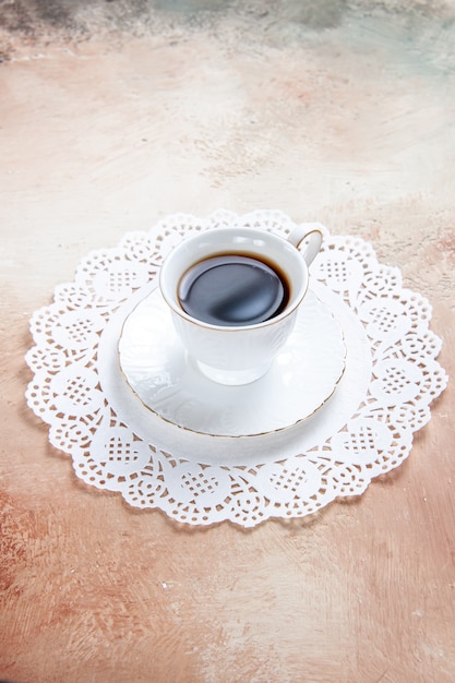 Foto gratuita vista verticale di una tazza di tè nero sul tovagliolo decorato bianco su colorato