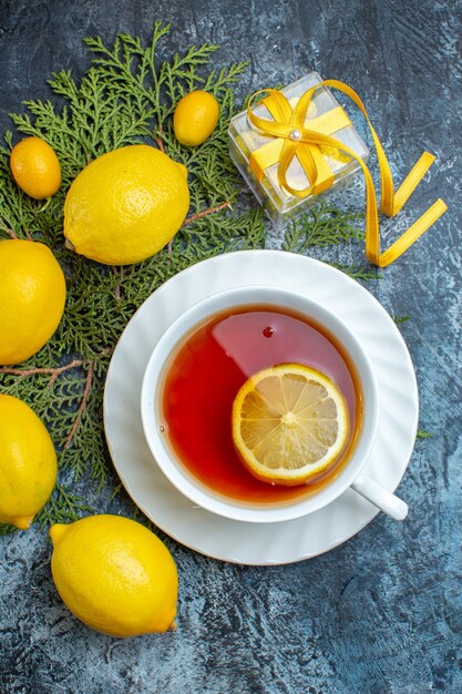 Foto gratuita vista verticale di una tazza di tè nero con limone e raccolta di agrumi freschi organici naturali su rami di abete su sfondo scuro