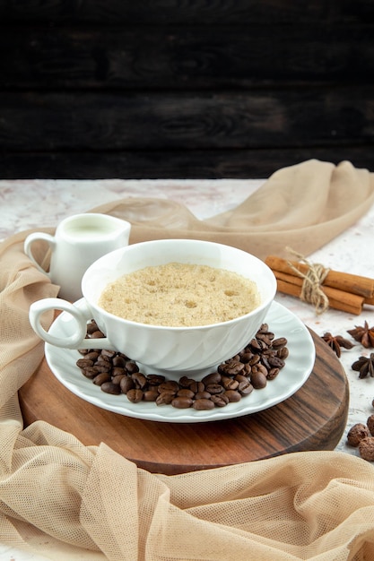 Free photo vertical view of a cup of coffee and beans ground cinnamon limes nude color towel on stained white table