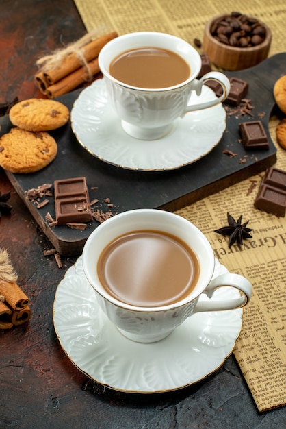 Vertical view of cup of coffee on wooden cutting board on an old newspaper cookies cinnamon limes chocolate bars