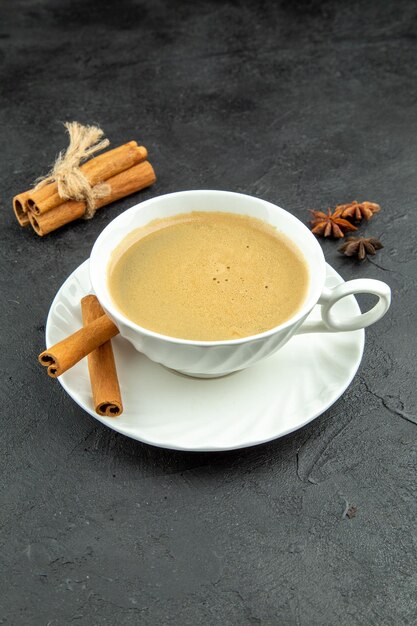 Vertical view of a cup of delicious coffee and cinnamon limes on dark backgorund