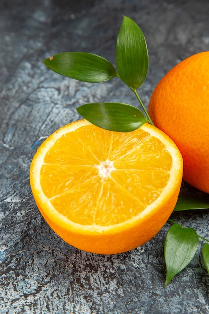 Вертикальный вид разрезанного пополам и целого свежего апельсина с листьями на сером фоне stock photo