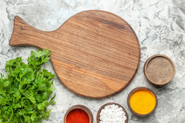 Vertical view of cutting board different spices and a bunch of green on white table