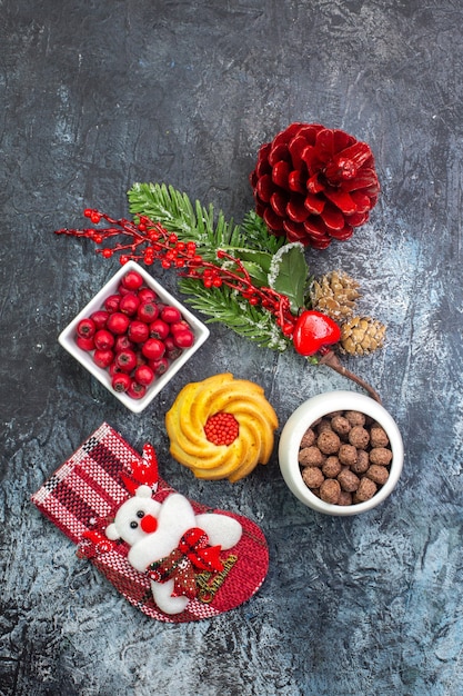 Vertical view of delicious biscuit decoration accessory santa claus sock and cornell in a bowl fir branches on dark surface