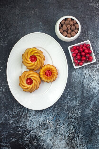 Vertical view of delicious biscuits on a white plate and cornel chocolate in bowls dark surface