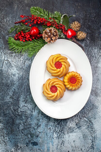 Vertical view of delicious biscuits on a white plate and new year decorations gift on dark surface