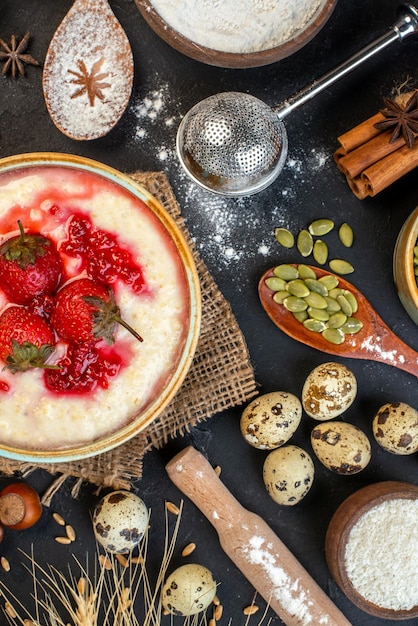 Vertical view of delicious breakfast served with strawberries jam in a bowl and cinnamon limes eggs spoons on dark color background