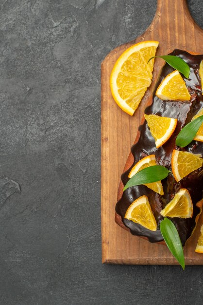 Vertical view of delicious cakes decorated with lemon and chocolate on cutting board on black table