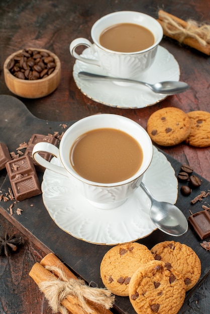 Вертикальный вид вкусного кофе в белых чашках на деревянной разделочной доске, печенье, корица, лайм, шоколадные батончики