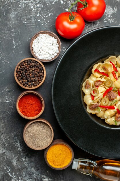 Vertical view of delicious conchiglie with vegetables greens on a plate and knife and different spices fallen oil bottle on gray table