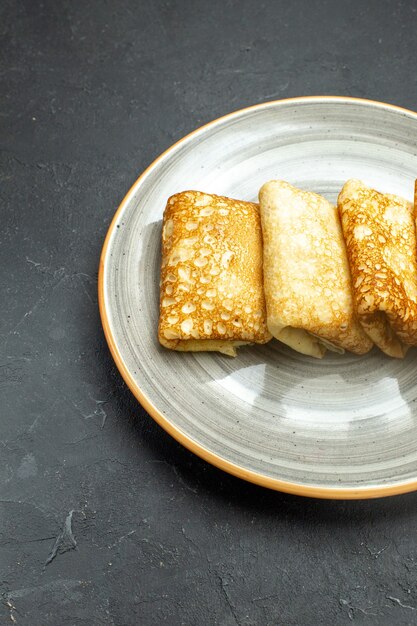 Vertical view of delicious meat-filled pancakes on a white plate on black background