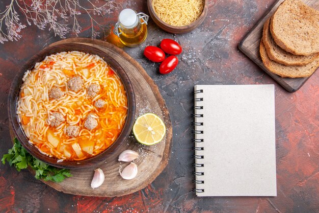 Vertical view of delicious noodle soup with chicken on wooden tary greens oil bottle garlic lemon tomatoes and notebook on dark background