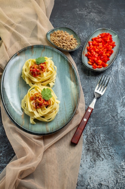 Вертикальный вид вкусной пасты на синей тарелке, подаваемой с помидорами и мясом на ужин на коричневом полотенце, его ингредиенты