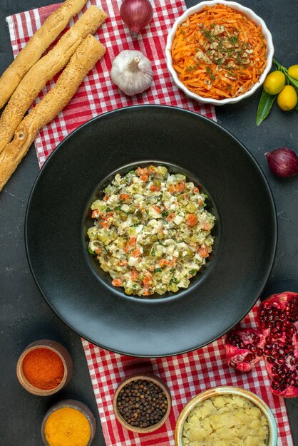 Vertical view of delicious salad garlic peppers salad pomegranates kumquats with stem on dark background