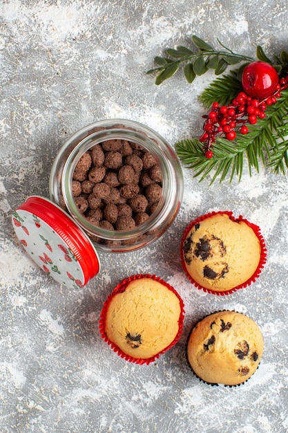 Vista verticale di deliziosi piccoli cupcakes e cioccolato in un vaso di vetro e rami di abete sulla superficie del ghiaccio