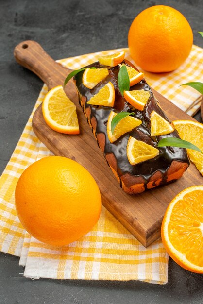 Vertical view of delicious soft cakes whole and cut lemons with leaves on dark table