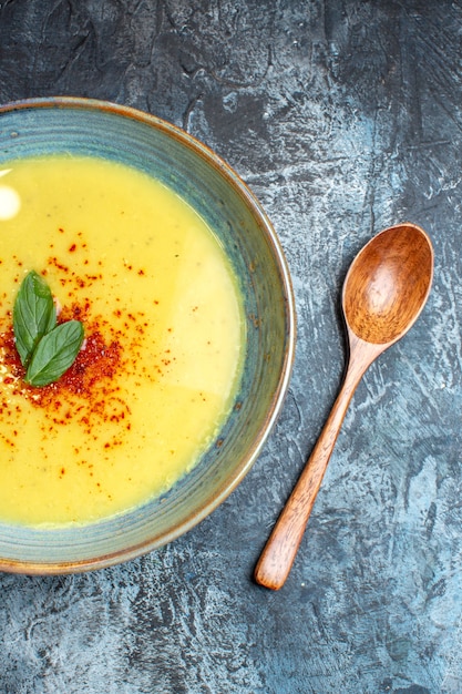 Foto gratuita vista verticale di una deliziosa zuppa servita con pepe e menta in una pentola blu accanto a un cucchiaio di legno su sfondo scuro