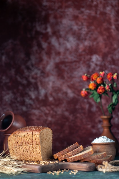 La vista verticale del pane nero dietetico picchia i grani sul tagliere di legno ciotole vaso di fiori su sfondo di colori misti marrone rossiccio