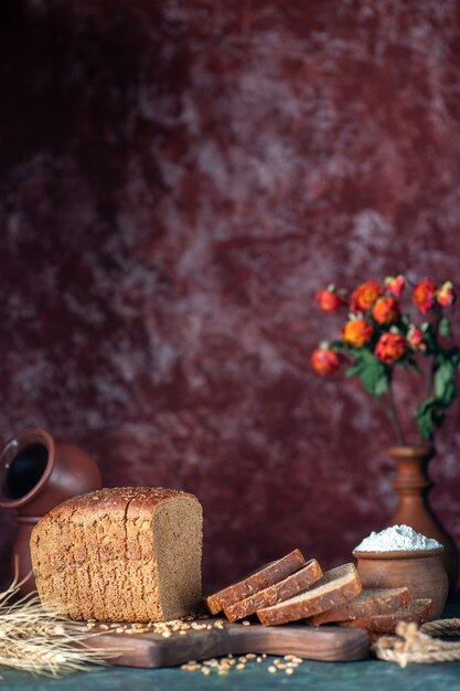 Vertical view of dietary black bread spikes wheats on wooden cutting board bowls flower pot on blue maroon mixed colors background