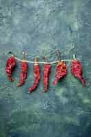 Free photo vertical view of dried red peppers tied up with rope on green black mixed colors background