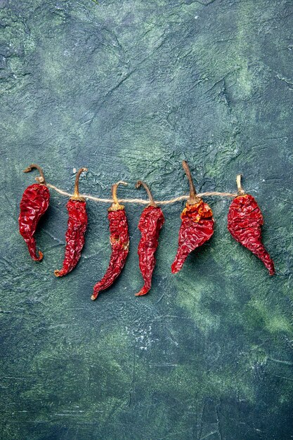Vertical view of dried red peppers tied up with rope on green black mixed colors background