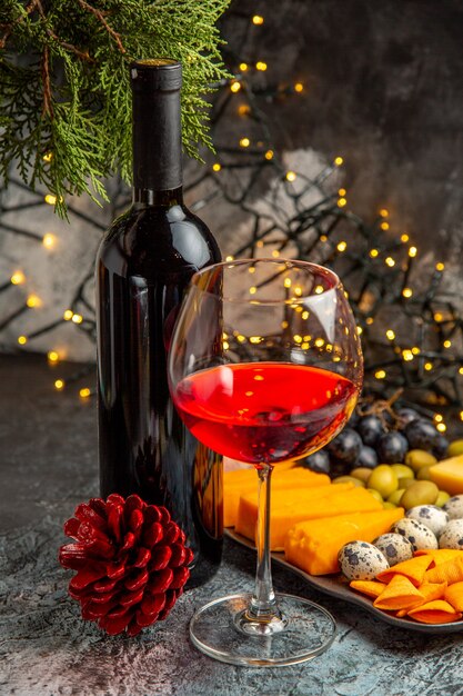 Vertical view of dry red wine in a glass and in a bottle next to snack and conifer cone on gray background