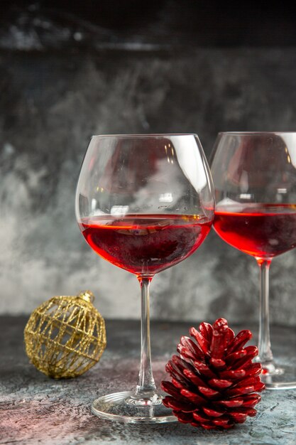 Vertical view of dry red wine in two glasses and decoration accessory conifer cone on gray background