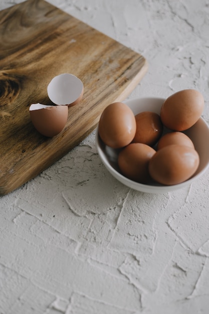 Vertical view of eggs in a bowl next to a chopping board on the table