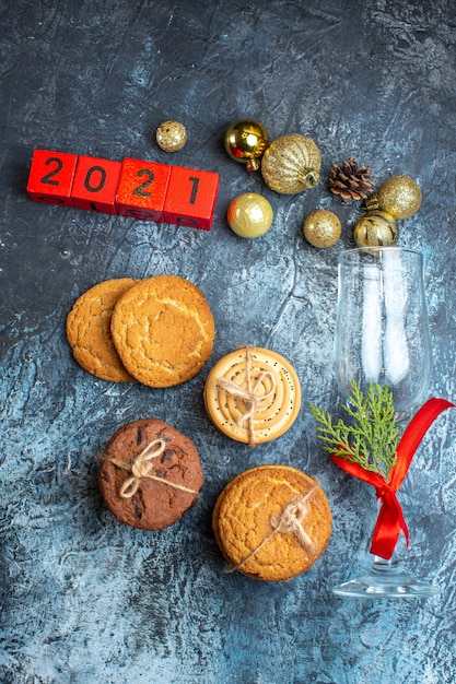 Vertical view of fallen glass goblet with red ribbon and decoration accessories next to stacked cookies numbers on dark background