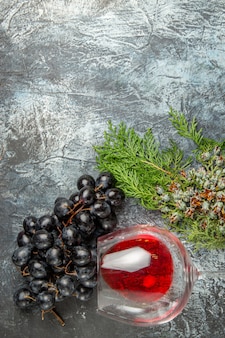 Vista verticale del bicchiere di vino rosso caduto e un mucchio di rami di abete d'uva nera su sfondo di ghiaccio
