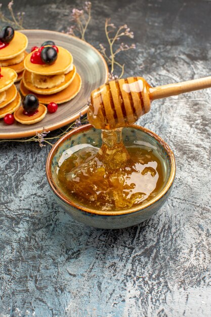 Vertical view of flowing honey from wooden spoonnd pancakes on large plate