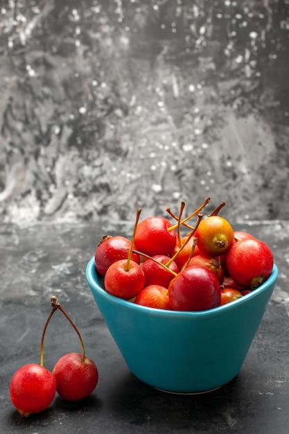 Free photo vertical view of fresh cherries inside and outside of blue basket on gray